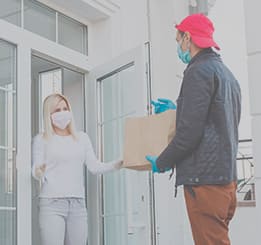 Mulher com máscara e luvas de proteção recebendo entregador de comida também com mascara e luvas.