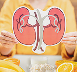 Mãos segurando desenho com alusão ao formato do rim cercado de alimentos benéficos ao combate à pedra nos rins