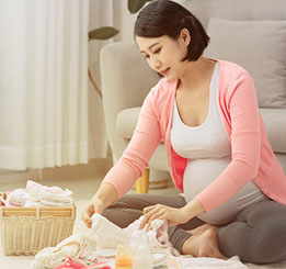 mulher japonesa, grávida, sentada de pernas cruzadas arrumando o enxoval do bebê