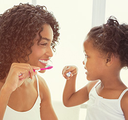 Mãe e filha afrodescendente escovando os dentes
