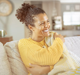 Mulher afrodescendente sentada no sofá enrolada sob o cobertor e rindo